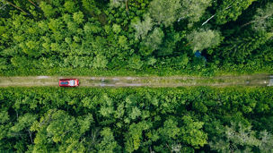 Aerial view of red car with a roof rack on a green summer forest country road in Finland