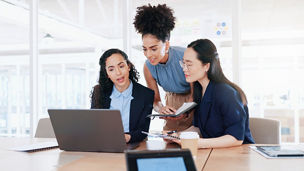 Business women, laptop and collaboration in office for marketing management, leader innovation or strategy research. Team meeting, employee support and tech manager or leadership idea discussion.