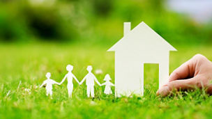 Hand holding a paper house and family on green grass