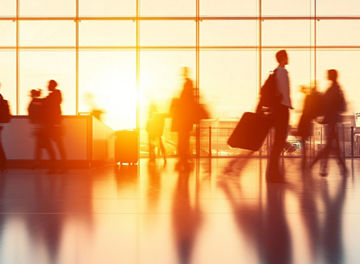 Silhouettes of travelers moving through a sunlit airport terminal, creating a dynamic panorama of modern mobility and global connectivity.
