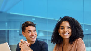 Two people smiling whilst sat at an office table in front of laptop