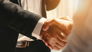 Two people in business attire shaking hands in a close-up, with focus on the handshake