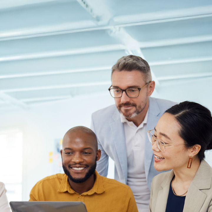 People smiling whilst gathered around an office table with a laptop