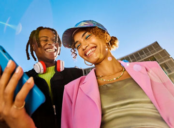 Two people in colourful clothing taking a selfie with a mobile phone with blue sky in the background