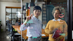 Two people stood up in an office space interacting with data on a transparent screen