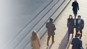 People walking on sidewalk next to dark stairs