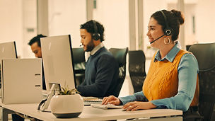 People wearing headsets sit at computers in an office workspace.