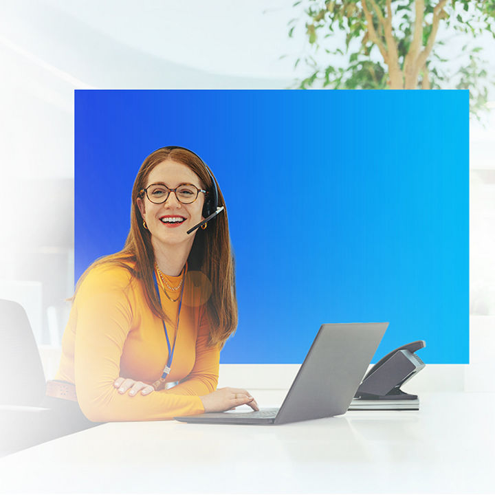 Person wearing a headset sitting at a desk using a laptop, with a blue panel background and a blurred office setting