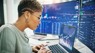 Person working on a laptop with multiple screens showing charts and financial data