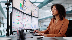Person working at a desk with multiple monitors displaying charts and dashboards