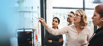 People looking at a transparent board whilst one person is writing on it with a marker pen