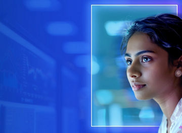 A person faces a computer monitor in an indoor office environment with blue lighting.