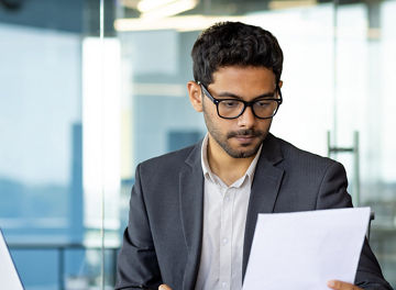Serious concentrated hispanic businessman financier on paperwork inside office, man in business suit at workplace reviewing and reading papers, contracts and accounts reports