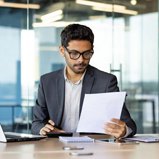 Serious concentrated hispanic businessman financier on paperwork inside office, man in business suit at workplace reviewing and reading papers, contracts and accounts reports