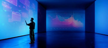 A person stood in a dark room pointing at data on a large screen