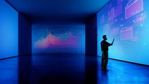 A person stood in a dark room pointing at data on a large screen