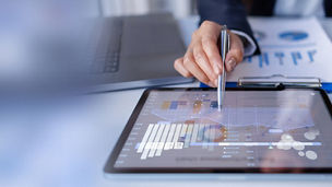 Person reviewing financial data and charts on a tablet in an office setting.