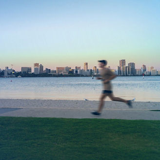 Person running along the Swan river with the Perth city skyline in the background