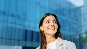 A person smiling whilst looking ahead with a glass building in the background