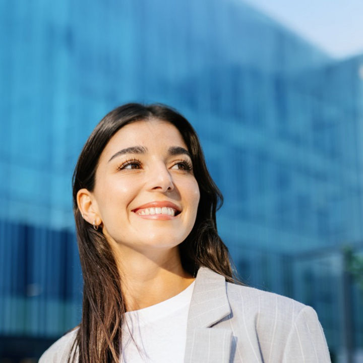 A person smiling whilst looking ahead with a glass building in the background