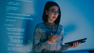 A person holding a tablet presenting with data being projected on the wall behind them