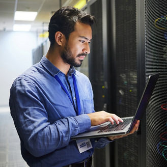 Person using a laptop to manage server equipment in a data center aisle..
