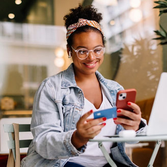 Person using a smartphone and credit card while sitting in a modern workspace.