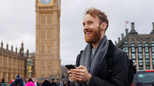 A person holding a smartphone while standing near the Palace of Westminster in London.