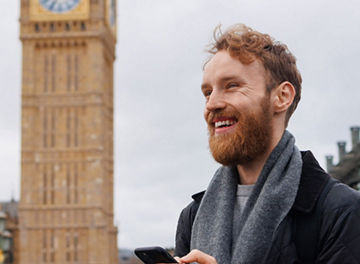 A person holding a smartphone while standing near the Palace of Westminster in London.