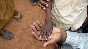 A thin refugee child's hand lies in the palm of an adults hand - Somalia refugee camp.