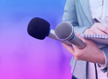 Person holding two microphones and a notepad and pen