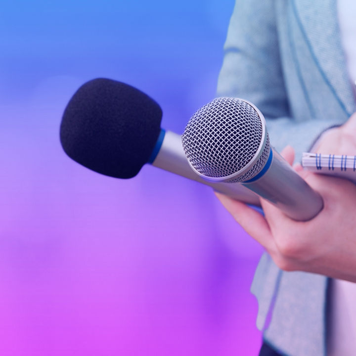 Person holding two microphones and a notepad and pen