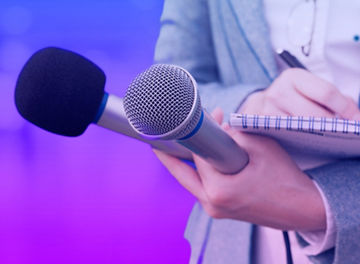 Person holding two microphones and a notepad and pen