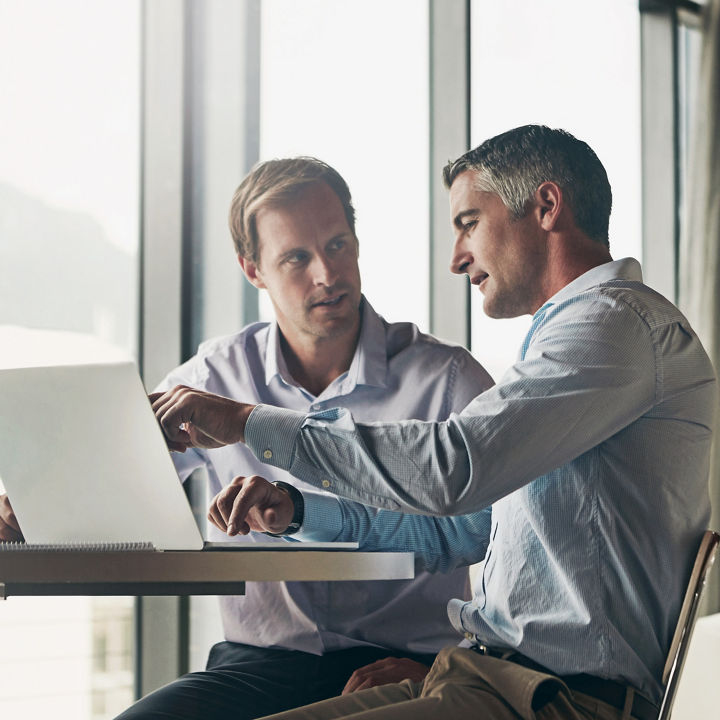 Business, men and discussion with laptop at office for advice, consultation and meeting on investment opportunities. Corporate, people and employees on website with report or feedback on share value.