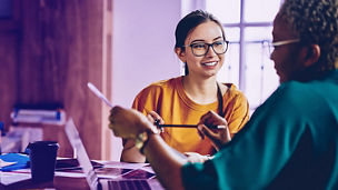 Carefree Caucasian employee in optical spectacles for provide eyes correction talking with dark skinned colleague discussing paperwork during collaborative briefing at desktop, business concept; Shutterstock ID 1958475958; purchase_order: marketing advisory assurance; job: Anne; client: AI campagne