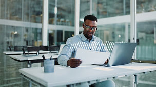 Professional reviewing documents and data on a laptop in a modern office.