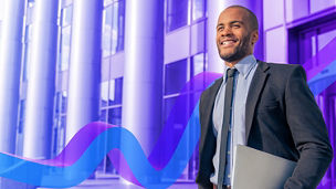 Homem sorridente de fato a sair de um edifício com um portátil na mão