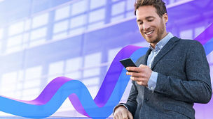 Businessman in a corporate environment looking at his mobile phone whilst smiling.