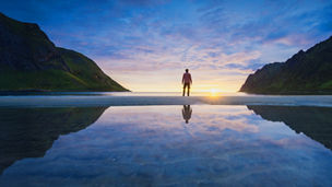 Reflected landscape of person standing between mountains looking at sunset over ocean