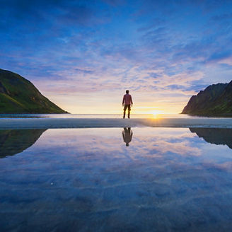 Reflected landscape of person standing between mountains looking at sunset over ocean
