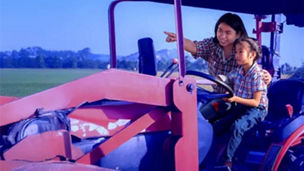 Fotografía de una mujer adulta conduciendo un tractor en el campo acompañada de una niña 