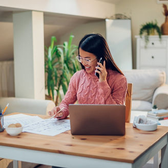 Young Vietnamese woman working in a home office and using a laptop and talking on a smartphone. Flexible workspace and working time. Beautiful Asian business female or student multitasking.