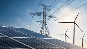 Solar panels and electricity pylons with wind turbines in the background under a blue sky
