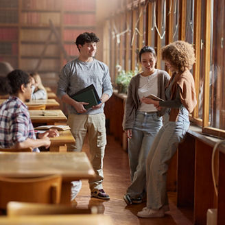 Group of happy diverse students enjoying on a break in library. One of them is using touchpad.