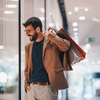 Man looking at a retail store window holding shopping bags