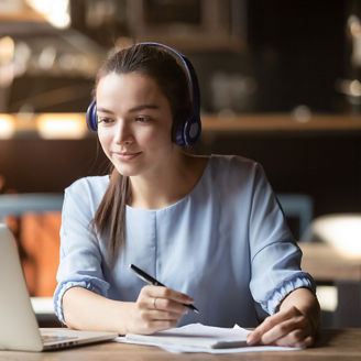 Focused woman wearing headphones using laptop in cafe, writing notes, attractive female student learning language, watching online webinar, listening audio course, e-learning education concept