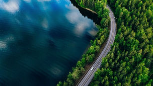 Aerial view of road between green summer forest and blue lake in Finland