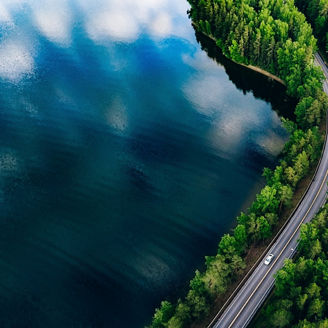 Aerial view of road between green summer forest and blue lake in Finland