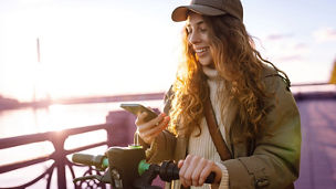 Activating electric scooter from smart phone. Happy woman driving electric scooter through the city. Ecological transportation concept. Travel, tourism concept. ; Shutterstock ID 2442003975; purchase_order: advisory assurance; job: anne; client: ai vertouwensmonitor