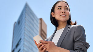 Frau mit Smartphone steht vor ein Hochhaus